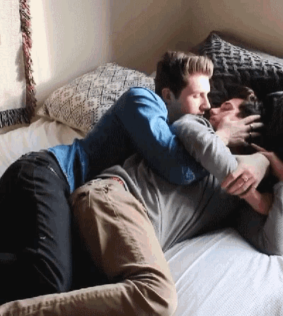 two men are laying on a bed hugging and kissing .