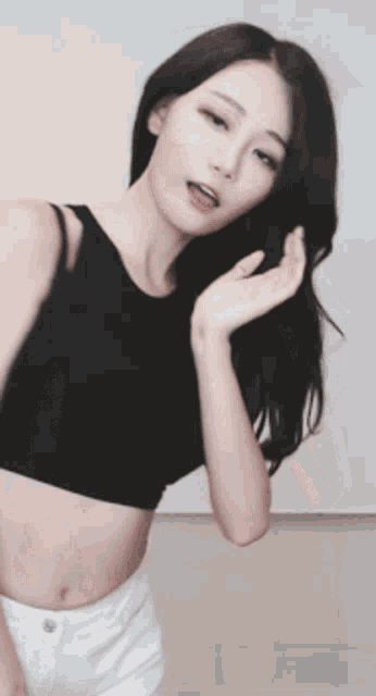 a woman in a black crop top and white shorts is dancing in front of a white wall .