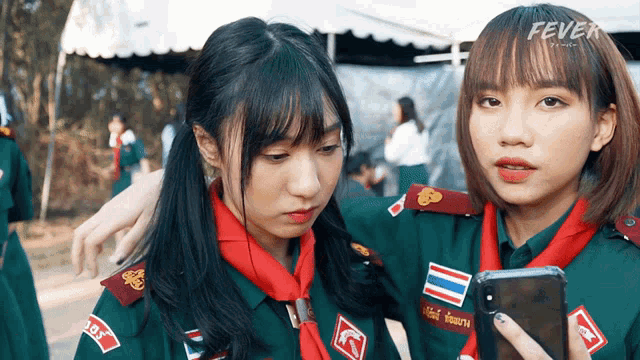 two girl scouts looking at a cell phone with the word fever on the bottom right