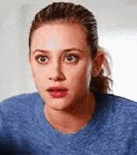 a woman is wearing a blue sweater and making a surprised face .