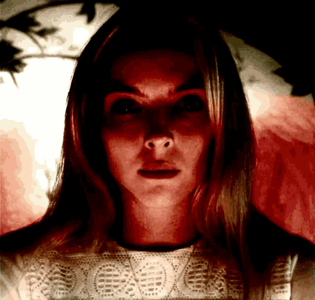 a close up of a woman 's face with red eyes and a white shirt