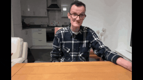 a man wearing glasses and a plaid shirt is sitting at a table