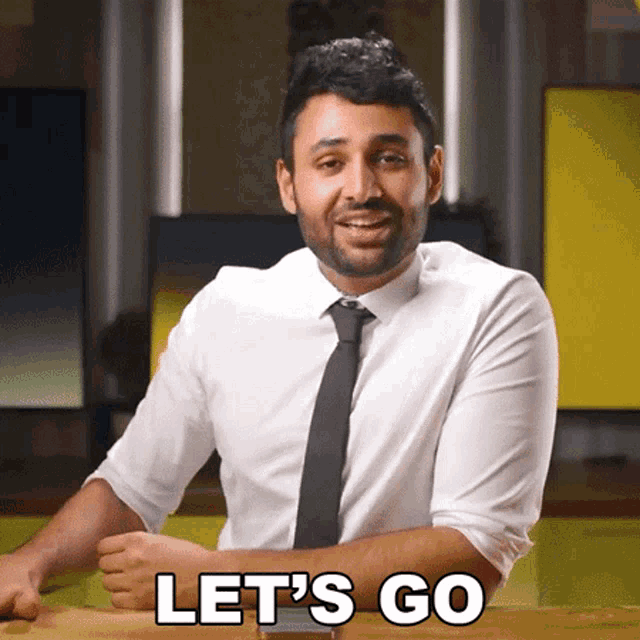 a man in a white shirt and black tie is sitting at a table and says let 's go