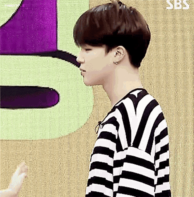 a young man wearing a black and white striped shirt is standing in front of a purple and green sign that says sbs