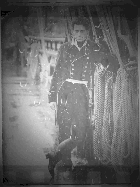 a black and white photo of a man in a military uniform standing next to ropes