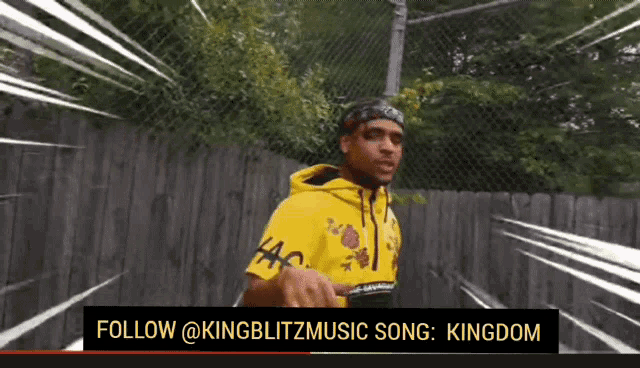 a man in a yellow hoodie stands in front of a fence