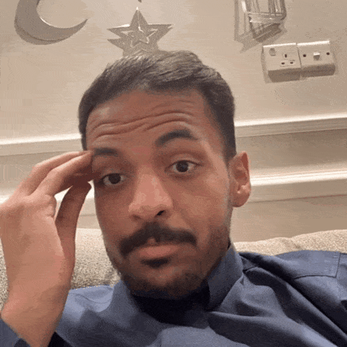 a man with a beard is sitting on a couch and touching his forehead with his hand