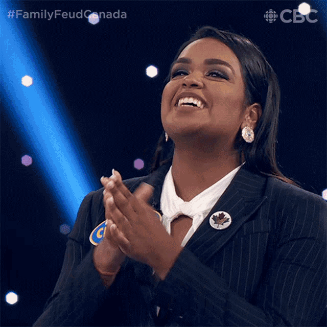 a woman in a suit is smiling and clapping while wearing a pin that says canada on it