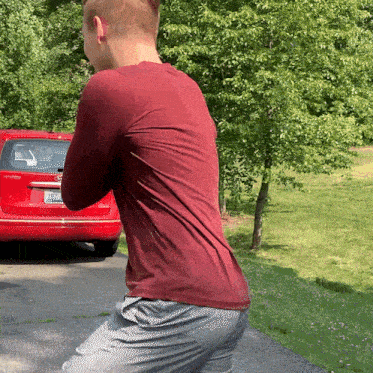 a man in a maroon shirt is standing in front of a red car with a license plate that says ' jd '