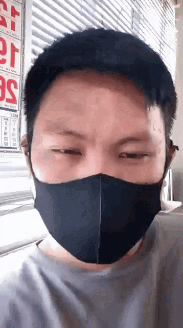 a man wearing a black mask looks at the camera with a sign in the background that says ' sg '