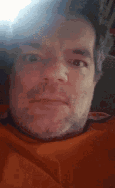 a man with a beard is making a funny face while wearing an orange shirt .