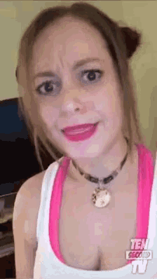 a woman wearing a pink tank top and a necklace is making a face .