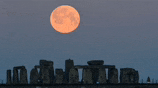 a full moon is rising over stonehenge in the distance