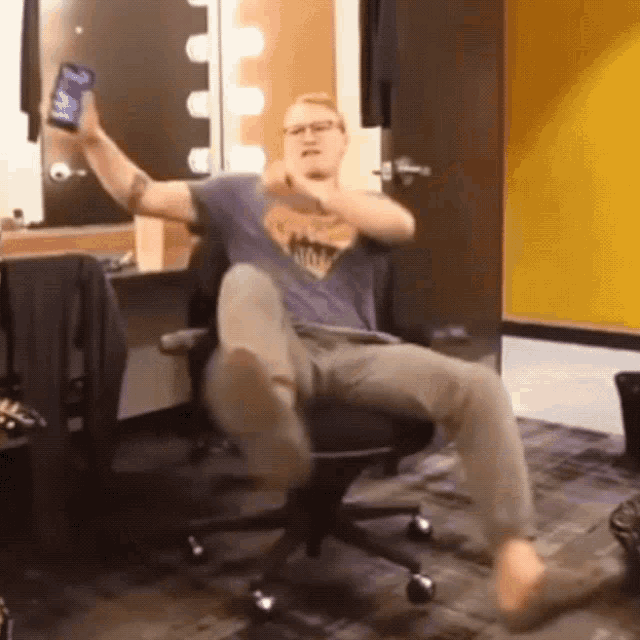 a man in a superhero shirt is sitting in an office chair with his feet up
