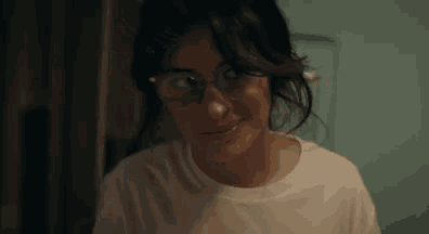 a woman wearing glasses and a white t-shirt is smiling .