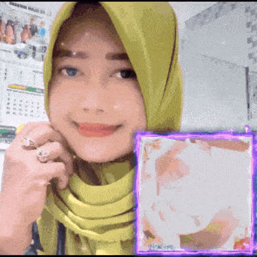 a woman wearing a green hijab is smiling next to a framed picture of her face