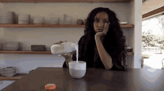 a woman is pouring milk into a cup .