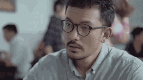 a man with glasses and a beard is sitting in a classroom with other people .