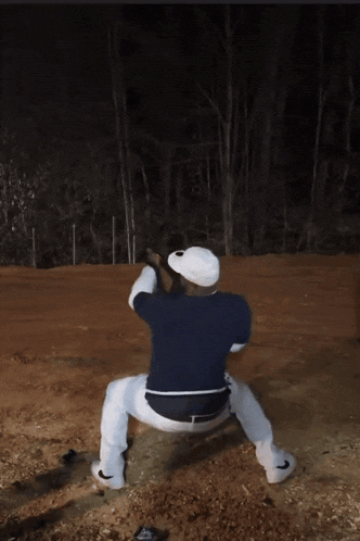 a man in a blue shirt and white pants is squatting down in the dirt