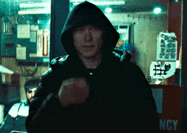 a man wearing a hooded jacket stands in front of a sign that says ncy