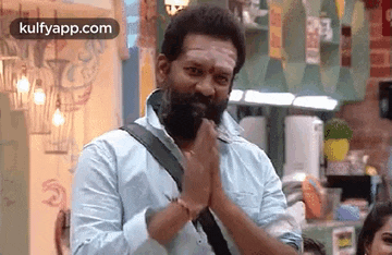 a man with a beard is standing in a room with his hands together .