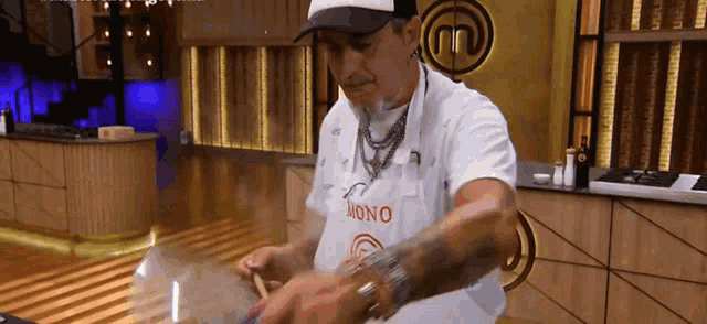 a man wearing an apron that says mono is standing in a kitchen .