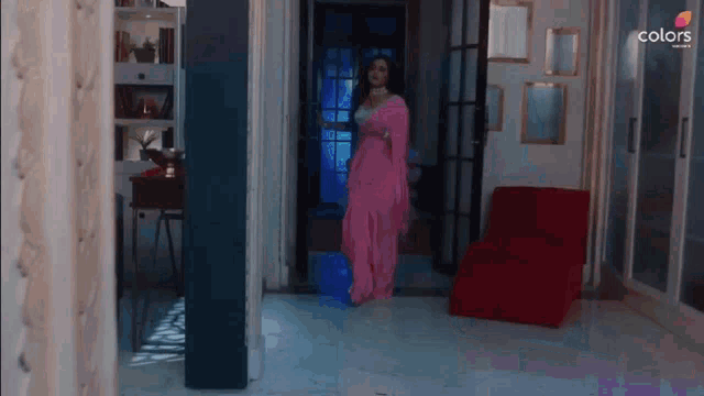 a woman in a pink saree is walking through a doorway .
