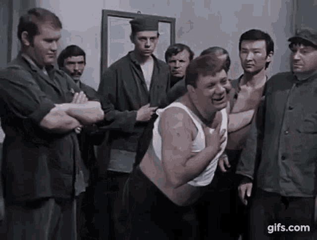 a group of men are standing around a man without a shirt in a room .