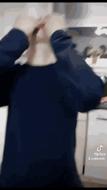 a man in a blue shirt is standing in a kitchen with his hands on his head