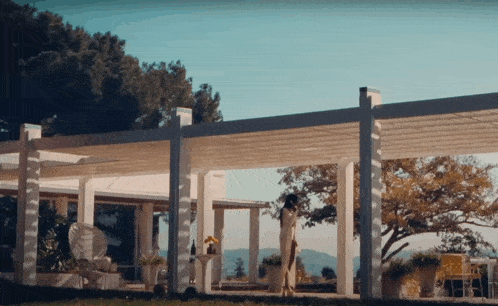 a woman is standing under a pergola in front of a white house
