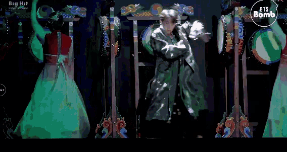 a woman in a red dress is dancing in front of a man in a black coat and a sign that says bts bomb on it