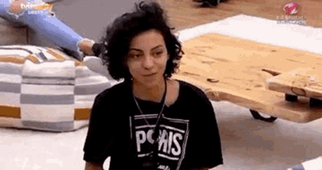 a woman wearing a black t-shirt with the word paris on it is sitting in front of a wooden coffee table .