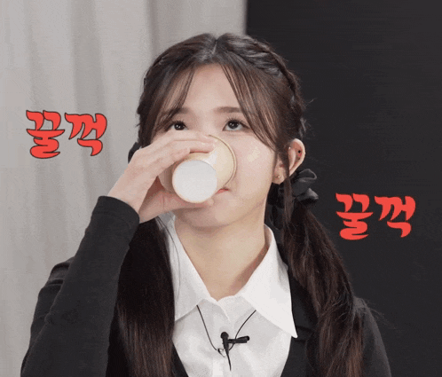 a girl is drinking from a paper cup with korean writing on the bottom
