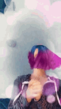 a woman with purple hair is wearing a striped shirt and holding balloons in front of her face .