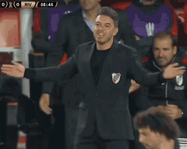 a man in a suit with a river plate on his jacket is standing on a soccer field with his arms outstretched .