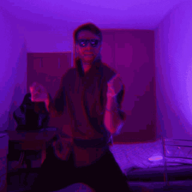 a man wearing sunglasses is dancing in a dark room with purple lights