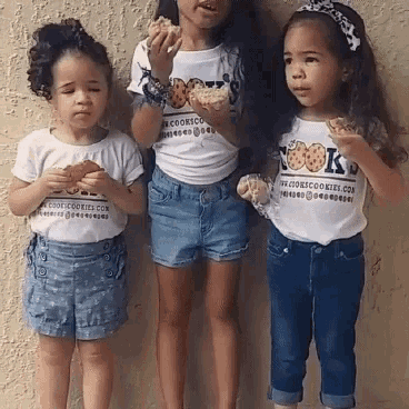 three little girls are standing next to each other eating cookies