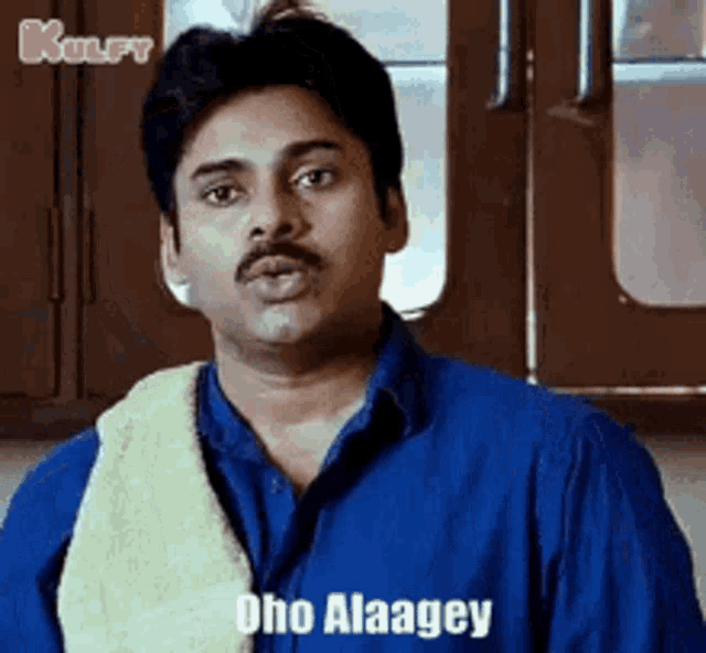 a man with a mustache is wearing a blue shirt and a towel around his neck and says dho alaagey .