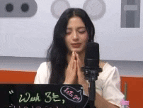a woman is praying in front of a microphone while sitting in front of a laptop .