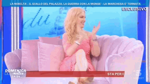 a woman in a pink dress is sitting on a pink couch on a television screen