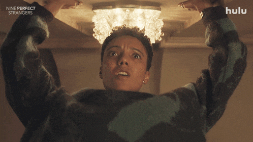 a poster for nine perfect strangers shows a woman looking up at a chandelier and asking what about me