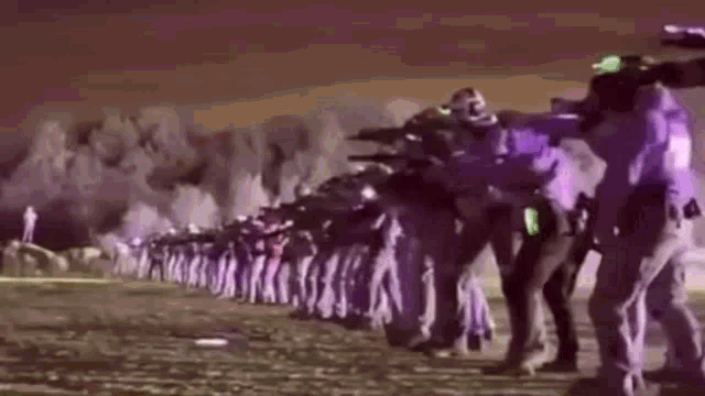 a group of police officers are standing in a line holding guns .