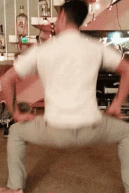 a man in a white shirt is squatting down in front of a bottle of liquor