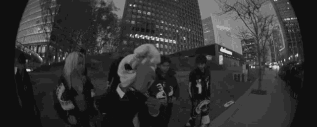 a group of people standing on a sidewalk in front of tall buildings