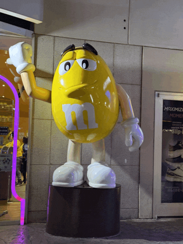 a statue of a yellow m & m holding a bottle of milk
