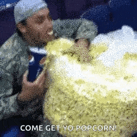a man is eating a large amount of popcorn and says come get yo popcorn .