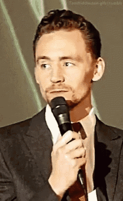 a man in a suit and tie is holding a microphone in front of his face .