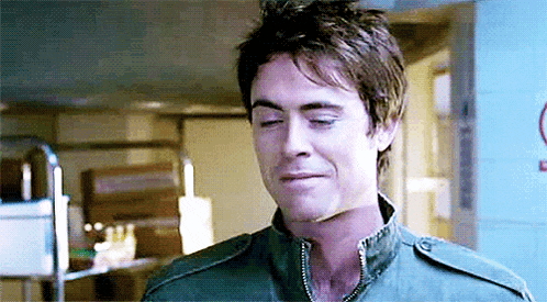 a man in a green jacket is making a funny face in a kitchen .