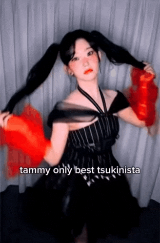 a woman in a black dress with pigtails is holding a red fan in her hand .
