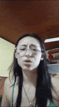a woman wearing glasses and a green top is making a face